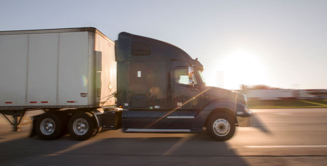 Semi-truck driving in front of the sun.
